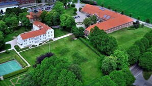 Eine Luftaufnahme eines Campus mit mehreren Gebäuden, grünen Rasenflächen und einem Tennisplatz.