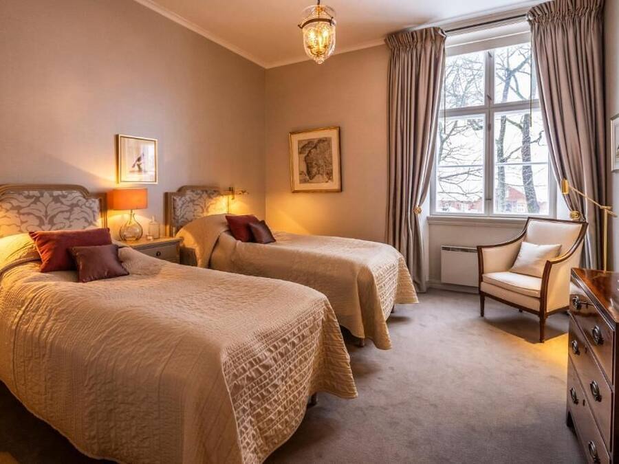 A hotel room with two beds, a chair, a dresser, and a window with curtains.