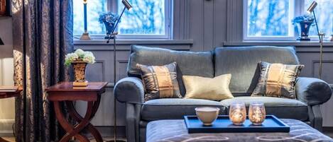 A cozy living room with a grey sofa, patterned ottoman, and a small side table with a vase and book.