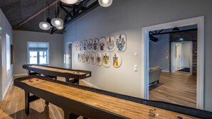 Ein Billardtisch in einem Raum mit Holzboden, einer Wand mit verschiedenen Kunstwerken und einer Tür zu einem weiteren Bereich.