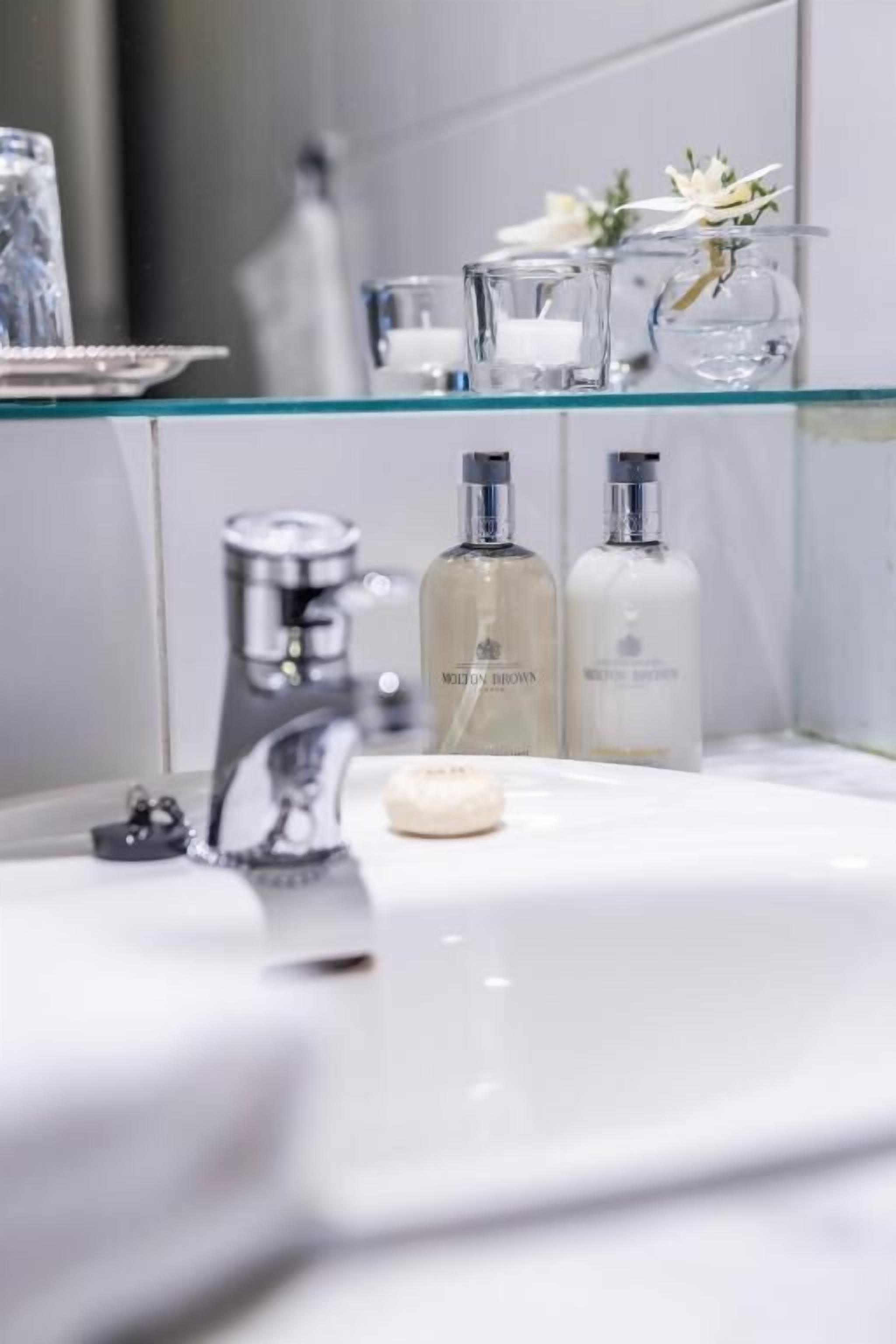 A bathroom with a glass shelf holding toiletries, a sink with a faucet, and a mirror.