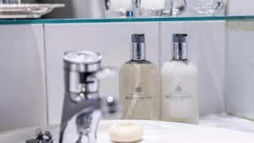 A bathroom with a glass shelf holding toiletries, a sink with a faucet, and a mirror.