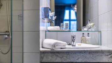 Ein modernes Badezimmer mit einer Glasablage, auf der ein Handtuch, zwei Gläser und Pflegeprodukte stehen.