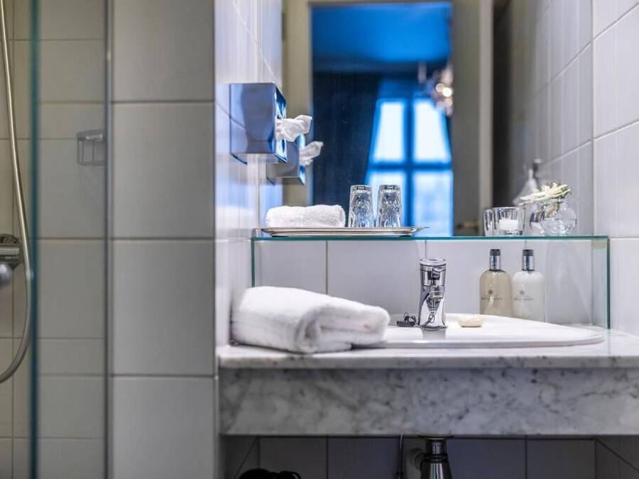 Ein modernes Badezimmer mit einer Glasablage, auf der ein Handtuch, zwei Gläser und Pflegeprodukte stehen.