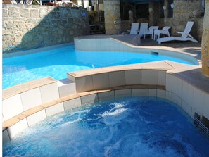 Ein Pool mit Whirlbereich, Steinwänden und weißen Liegestühlen.