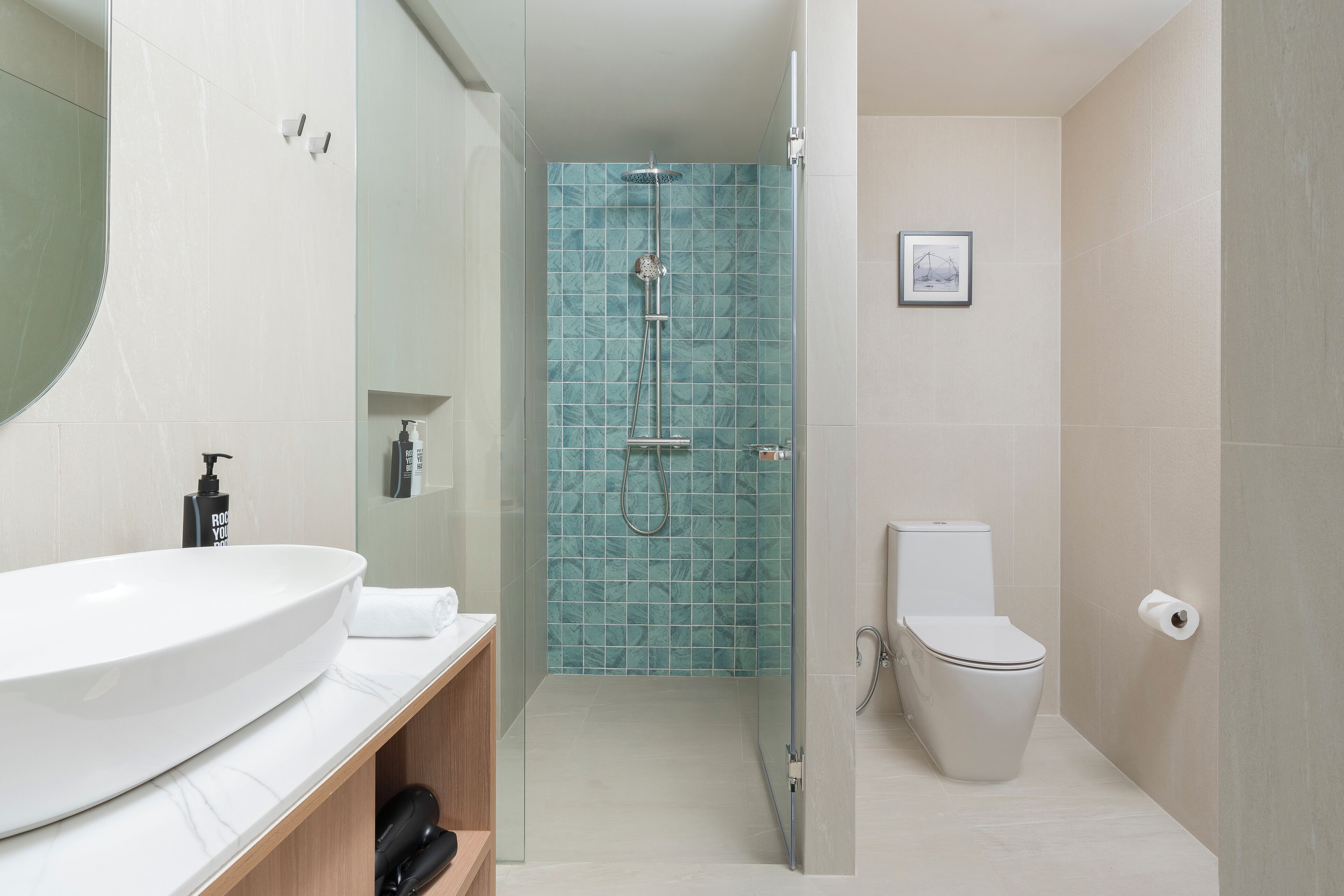 Une salle de bain avec un grand lavabo blanc, une cabine de douche en verre, des toilettes et un tableau encadré au mur.
