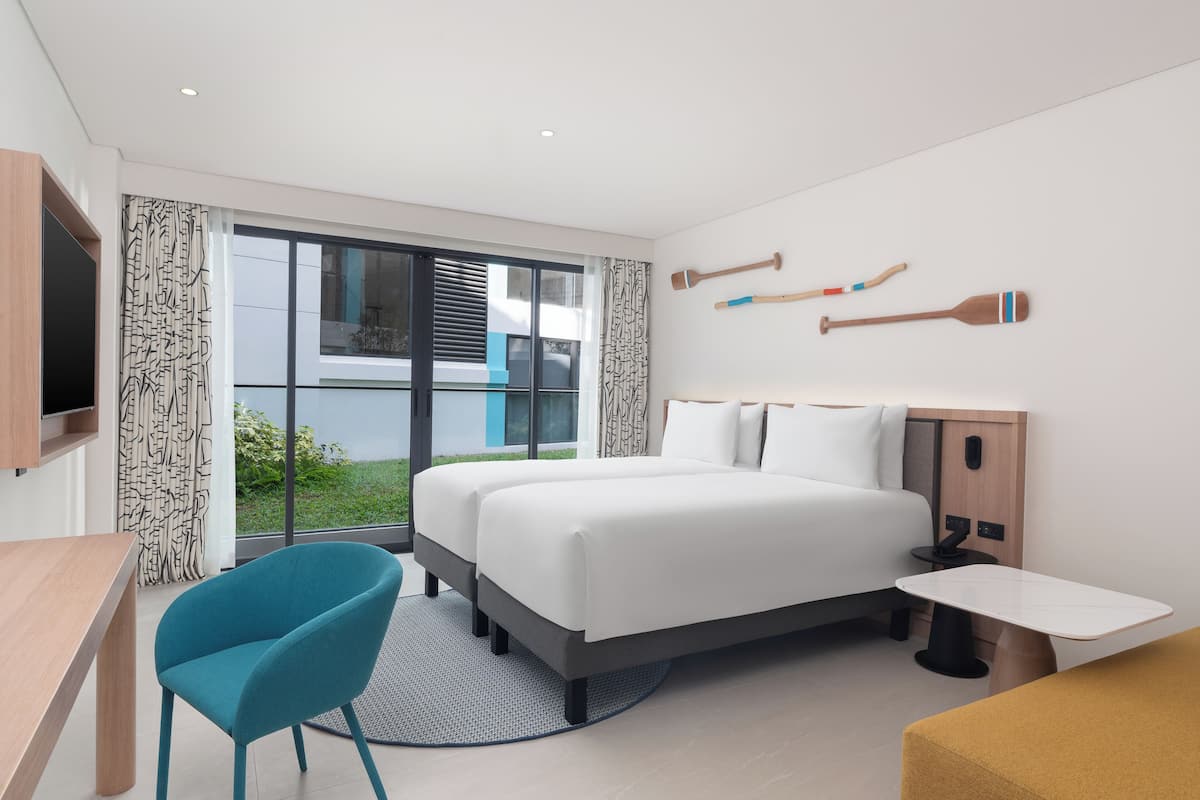 Une chambre d’hôtel moderne, dotée d’un grand lit, d’un bureau, d’une chaise et offrant une vue sur l’extérieur grâce à une grande fenêtre.