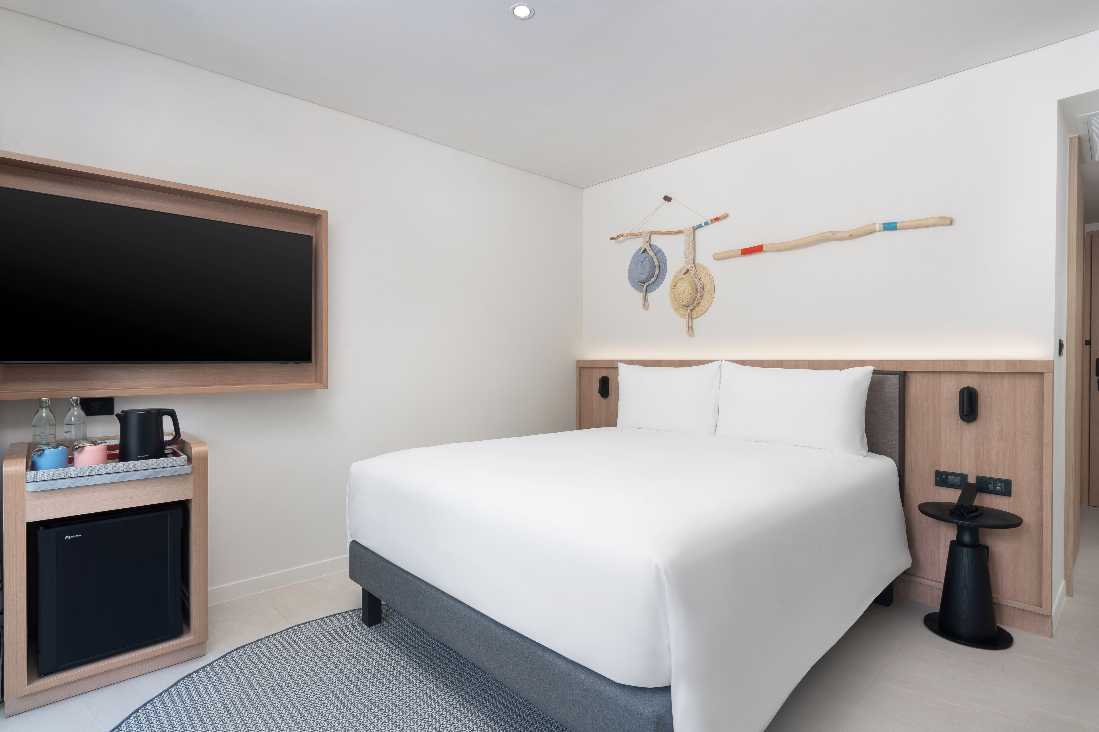 Una habitación de hotel moderna con una cama grande, un televisor de pantalla plana, un escritorio pequeño con un hervidor y una decoración de pared original.