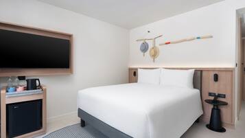 Una habitación de hotel moderna con una cama grande, un televisor de pantalla plana, un escritorio pequeño con un hervidor y una decoración de pared original.