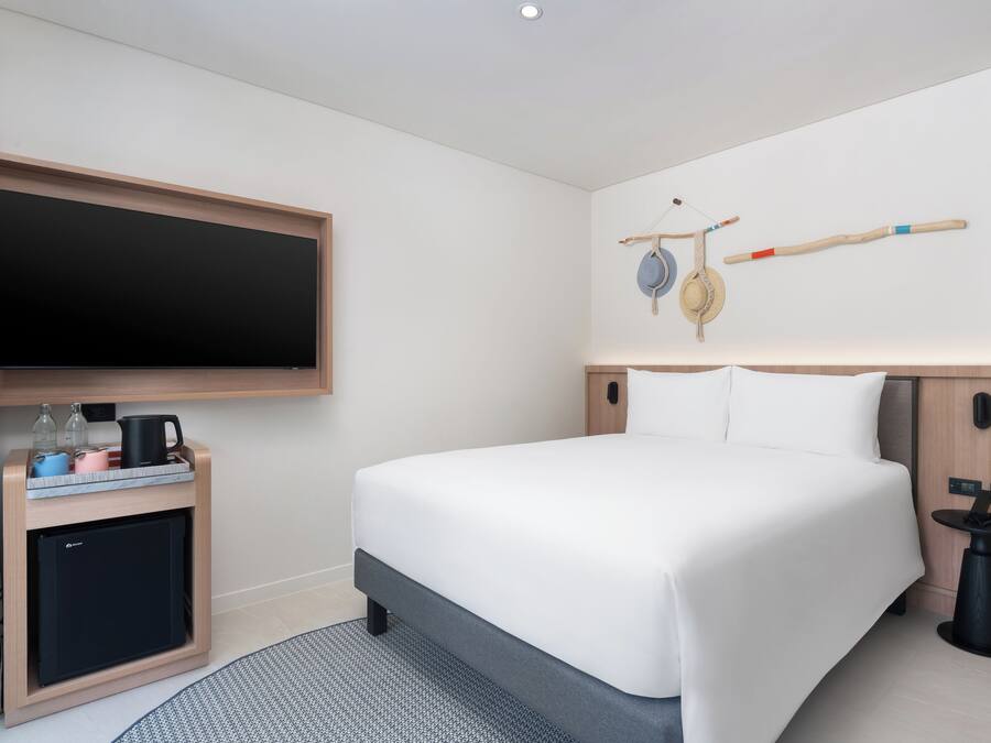 Una habitación de hotel moderna con una cama grande, un televisor de pantalla plana, un escritorio pequeño con un hervidor y una decoración de pared original.