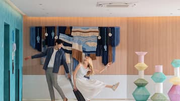 Un hall d’hôtel moderne avec un mur en bois, un mur d’accent bleu et une décoration murale. On y trouve des vases géométriques aux couleurs vives, disposés sur le sol.