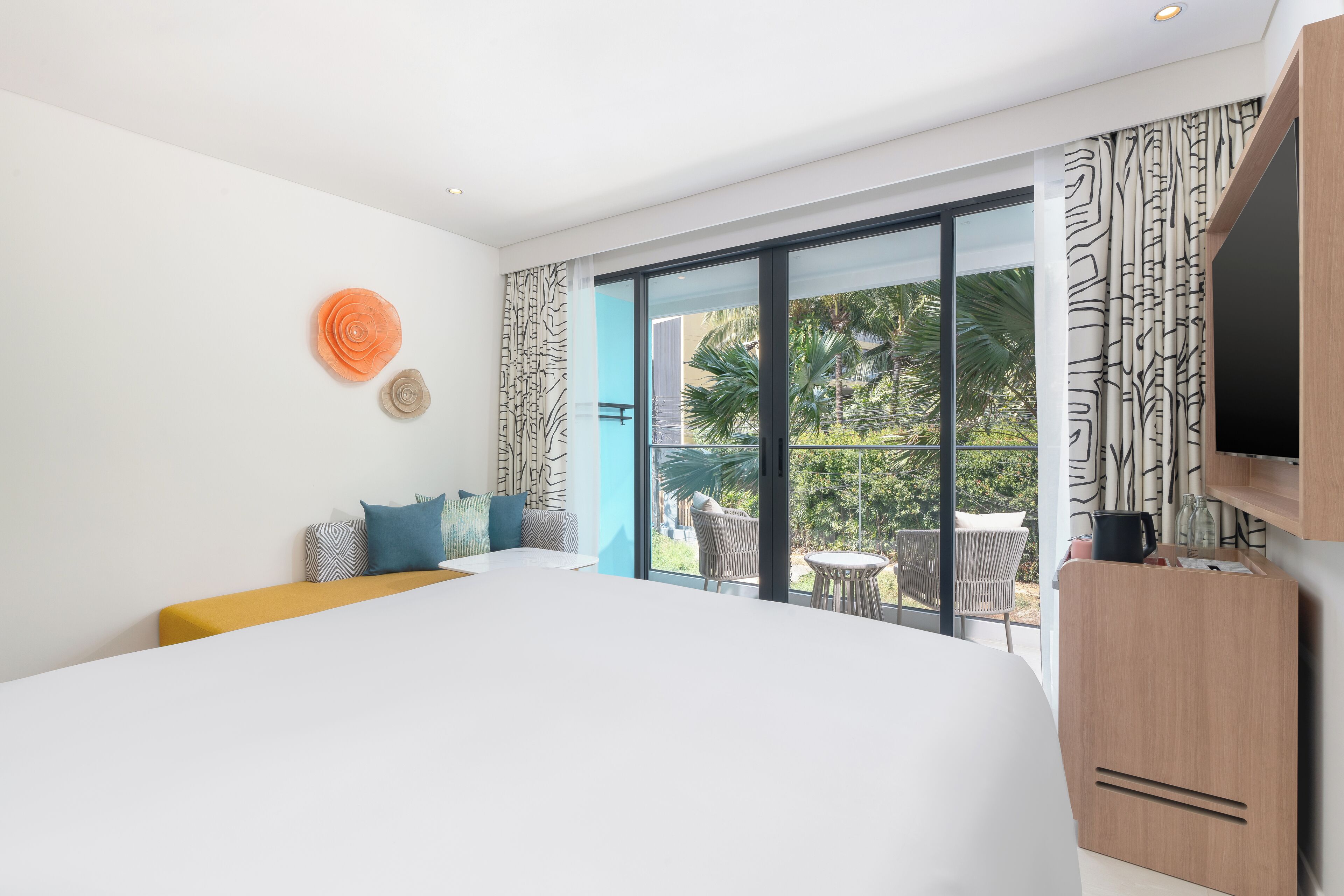 Habitación de hotel moderna con una cama grande, un televisor, un balcón con mobiliario exterior y vistas a zonas verdes.