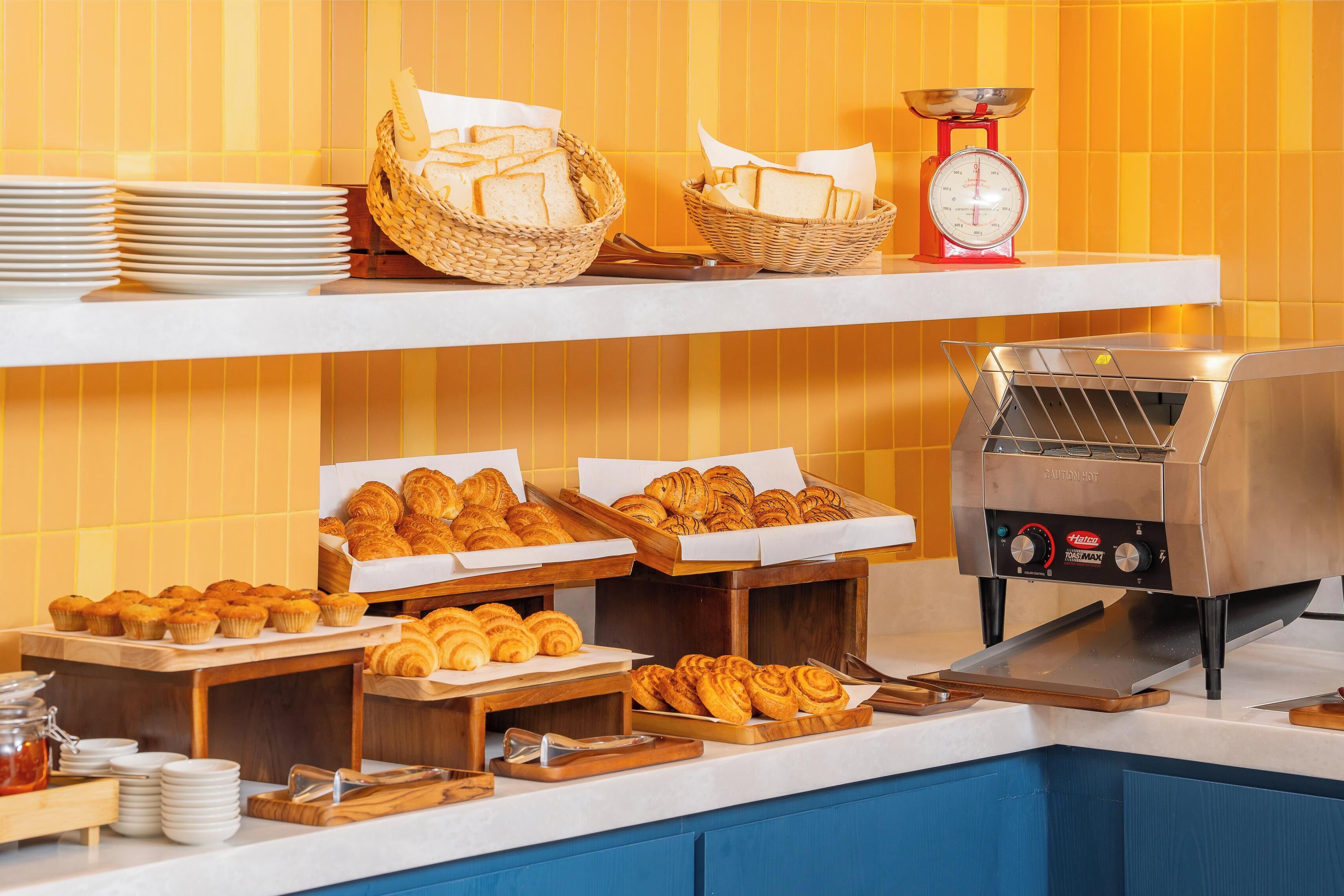 A buffet setup with bread, pastries, and a bread slicer.