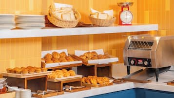 Una mesa de buffet con pan, bollería y un cortador de pan.
