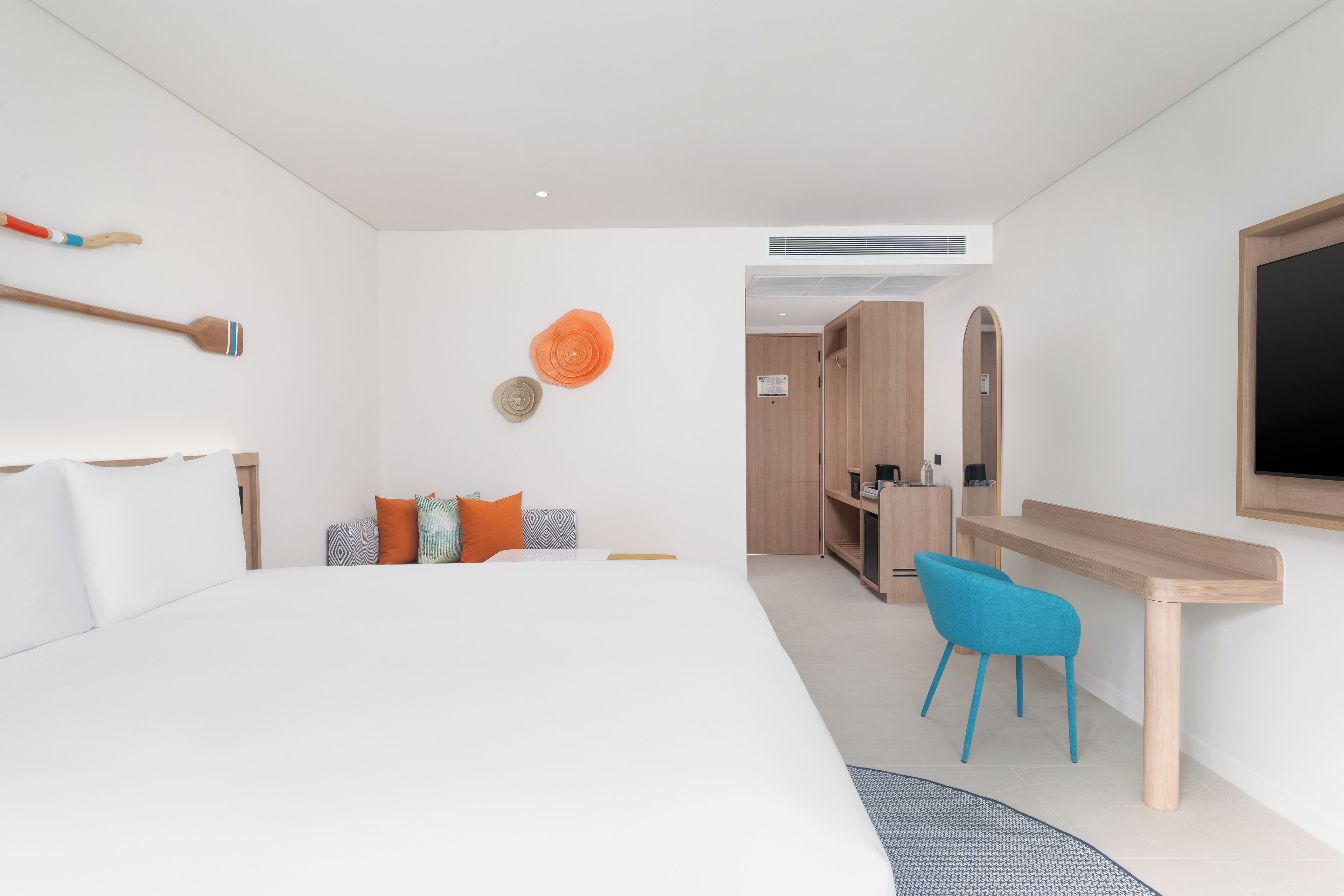 A modern hotel room with a large bed, a desk, a chair, and a TV.