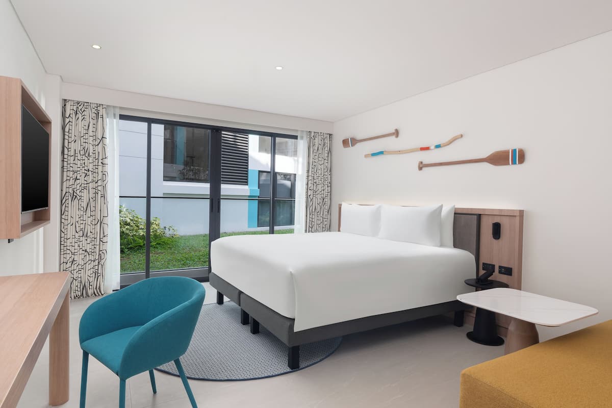 Une chambre d’hôtel moderne, dotée d’un grand lit, d’un bureau, d’une chaise et offrant une vue sur l’extérieur.
