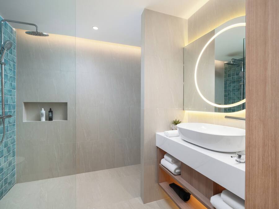 Un baño moderno con un lavamanos grande, un espejo con luz circular y una zona de ducha.