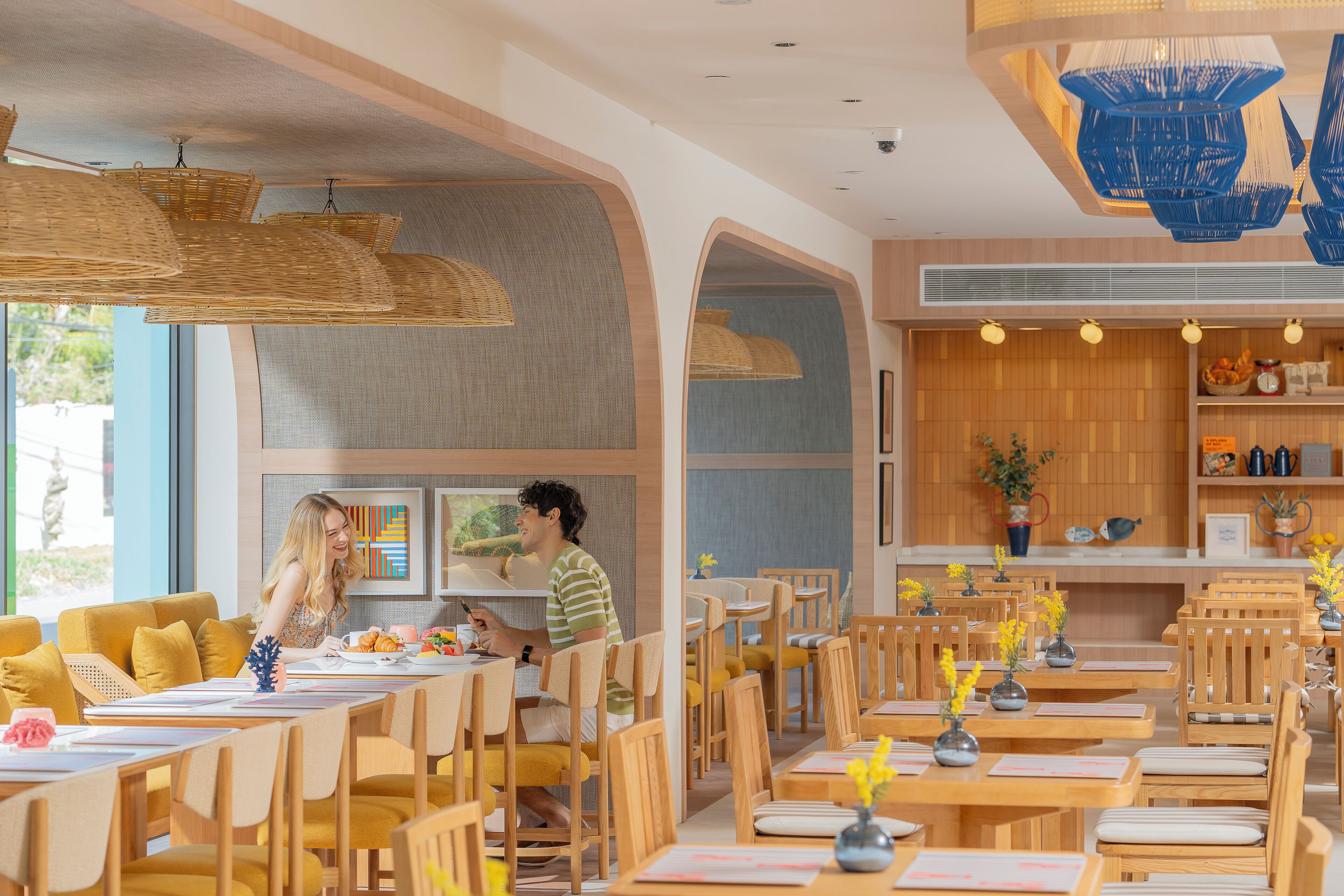 A restaurant with wooden tables and chairs, hanging wicker lamps, and a view of the outdoors.