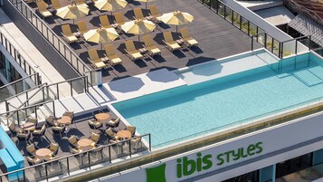 A rooftop pool area with sun loungers and umbrellas, a pool, and a sign reading "ibis styles".