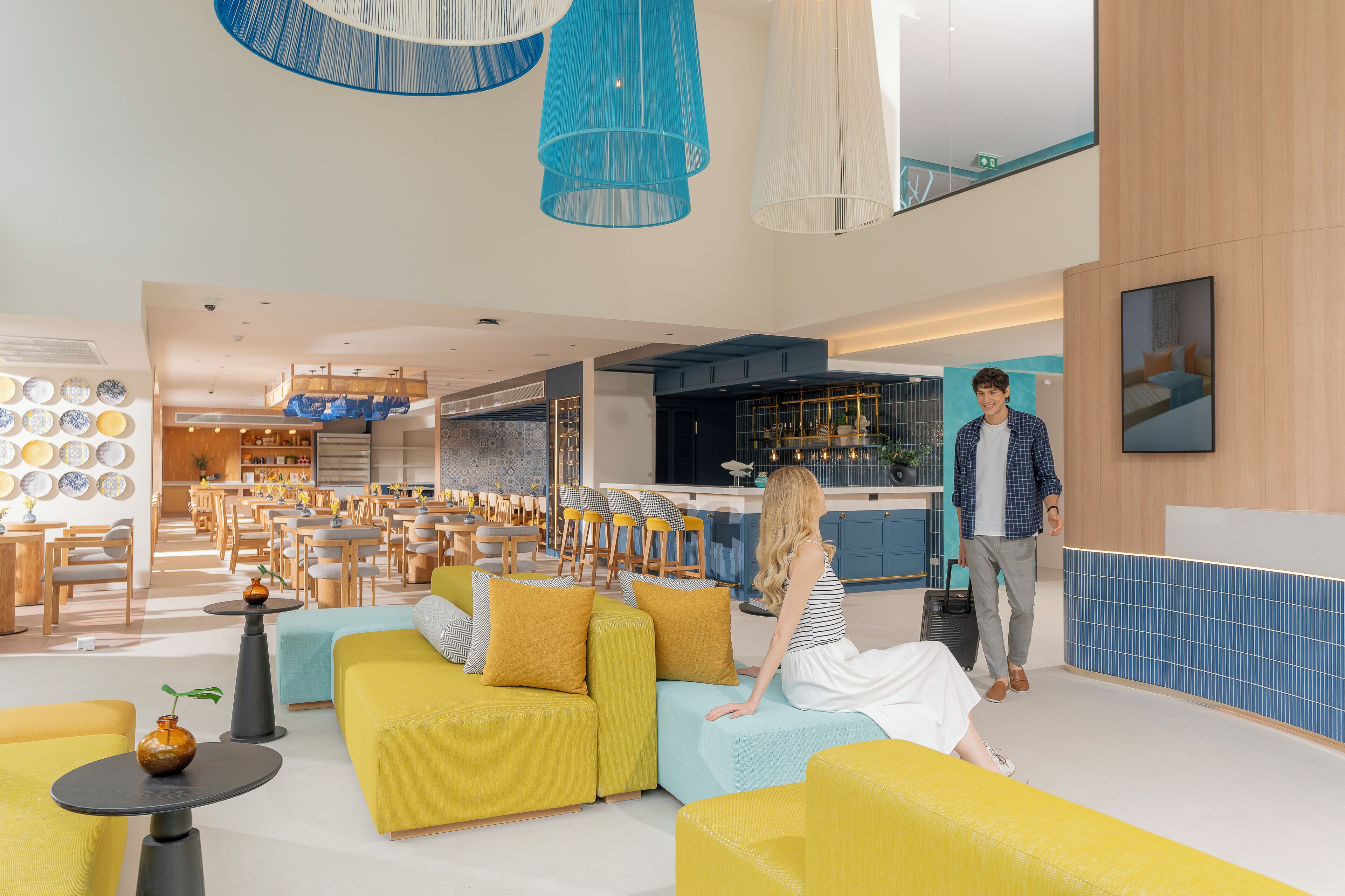 A modern hotel lobby with yellow sofas, a kitchen area, and a dining space.