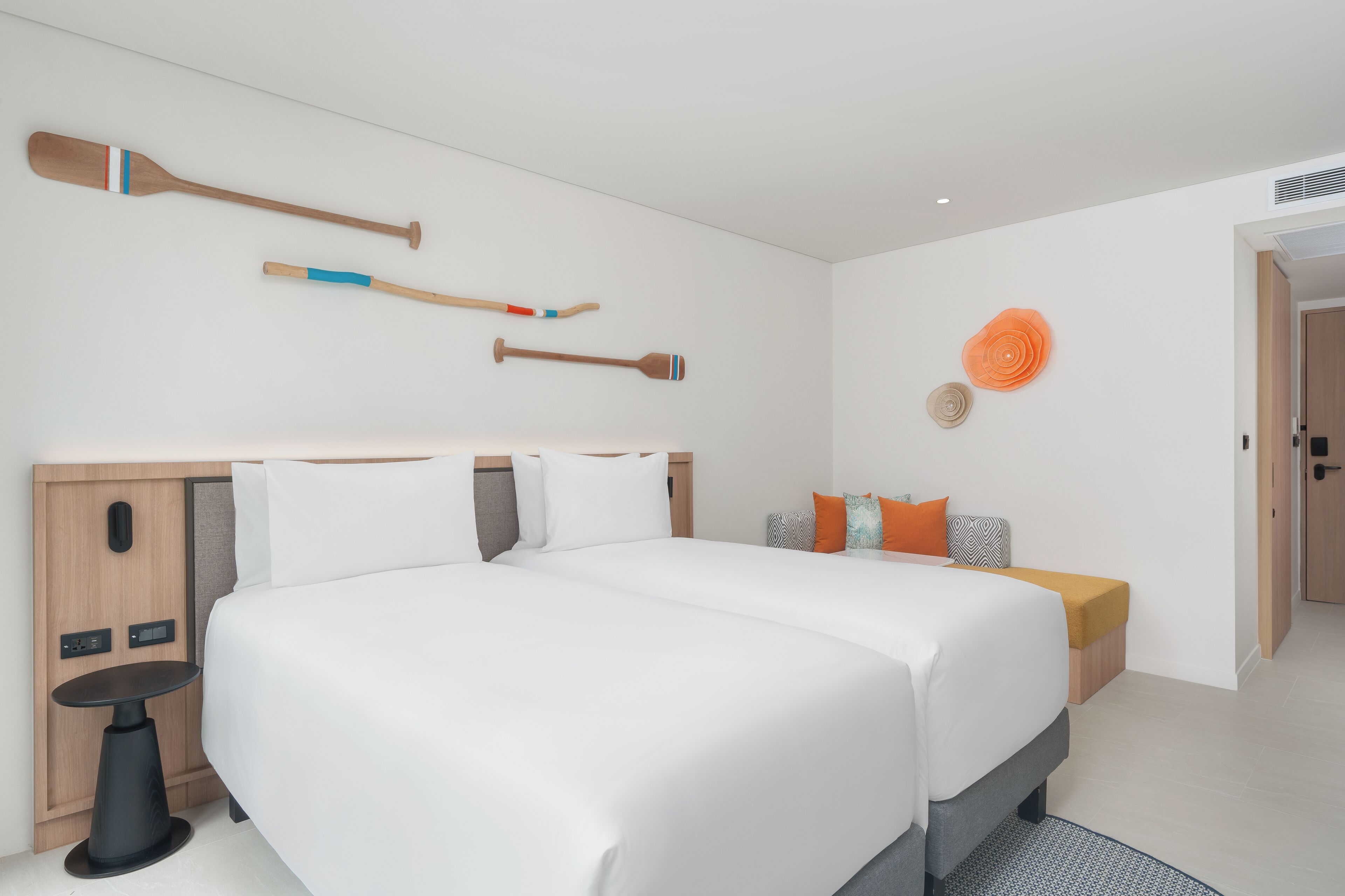 Une chambre d’hôtel moderne dotée d’un grand lit, d’une table de chevet, d’un téléviseur fixé au mur et d’un petit coin salon avec des coussins.