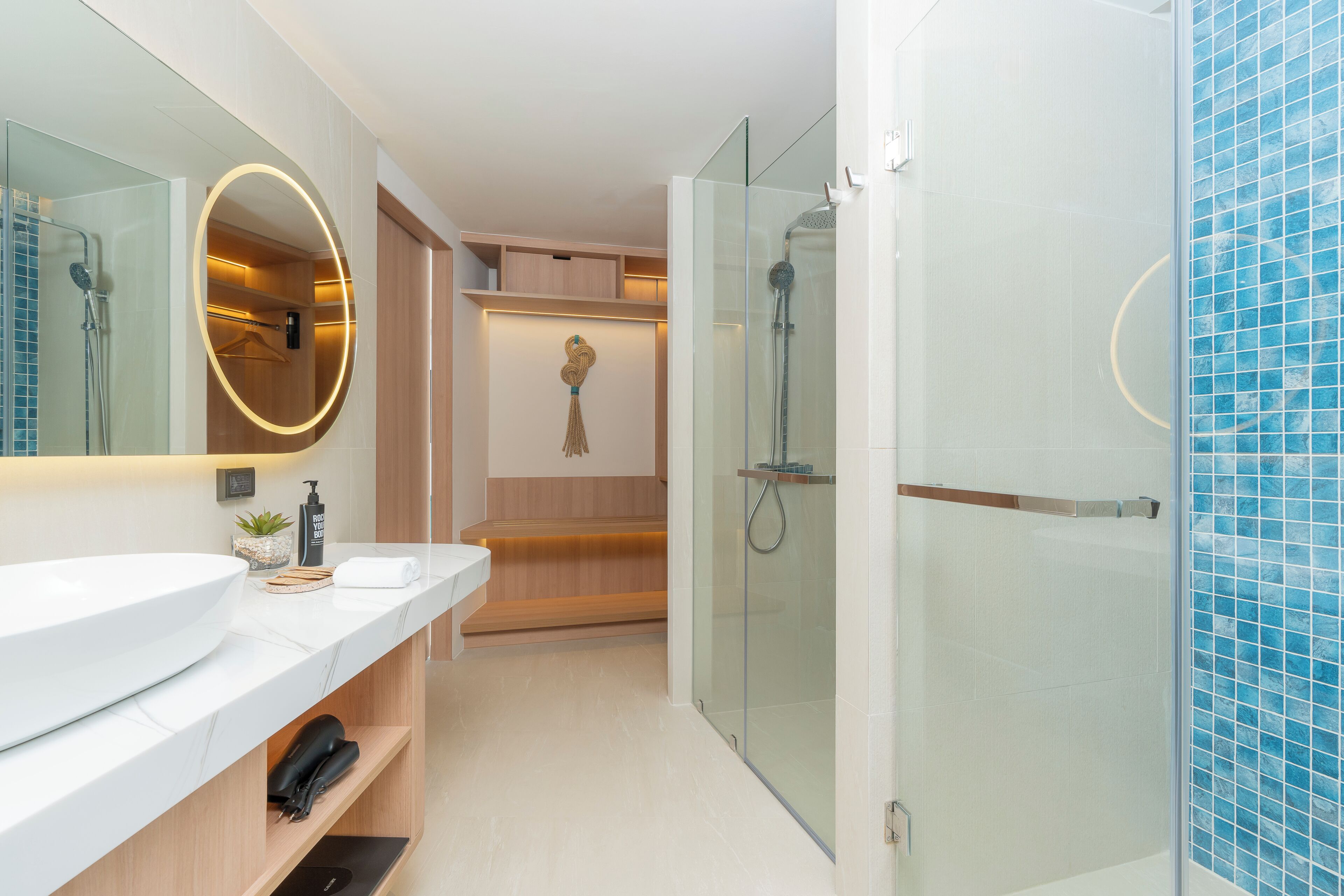Een moderne badkamer met een grote spiegel, een witte wastafel, een douche met glazen wanden en een wand betegeld met blauwe tegels.