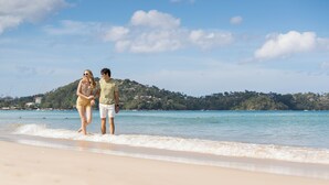 A couple standing on a beach with a clear sky and a distant hill.