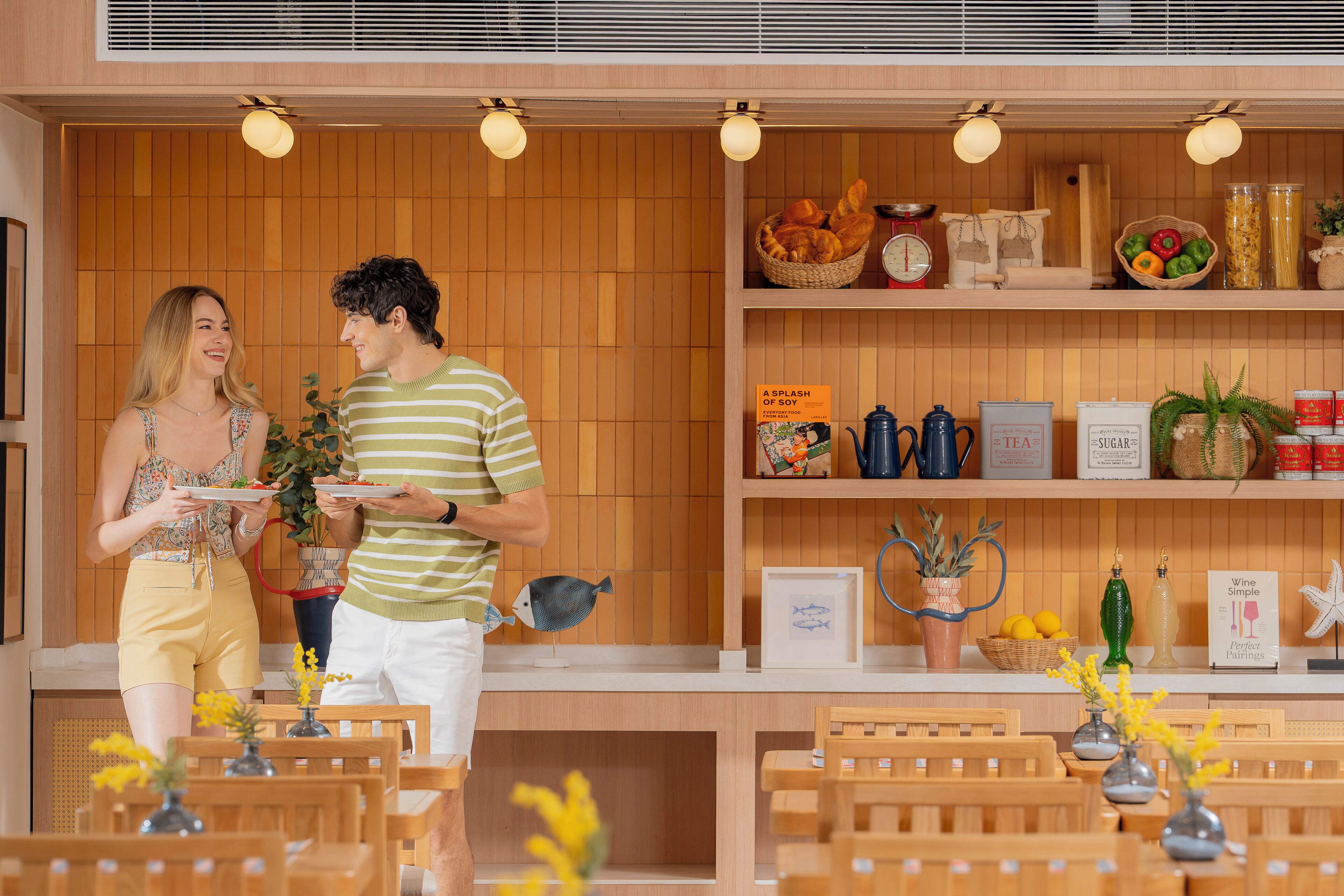 L’intérieur d’un restaurant présente des murs lambrés, un comptoir où sont exposés divers plats, et un espace où sont disposées des tables et des chaises.