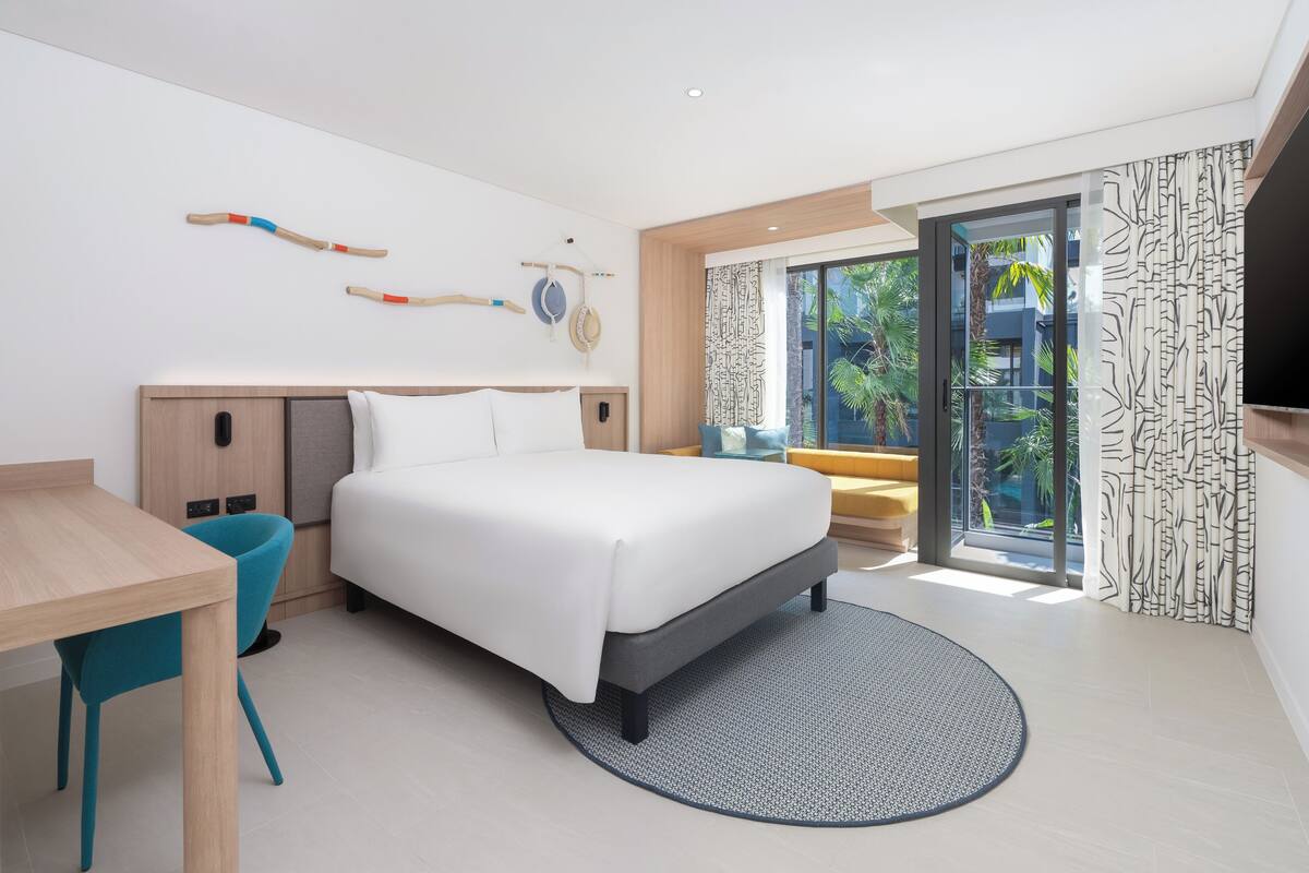 Une chambre d’hôtel moderne équipée d’un lit, d’un bureau, d’une chaise, d’une télévision et offrant une vue sur l’extérieur.