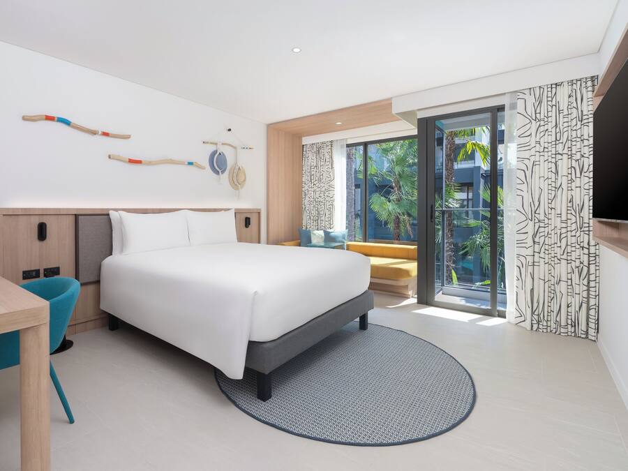 Habitación de hotel moderna con cama, escritorio, silla, televisor y vistas al exterior.