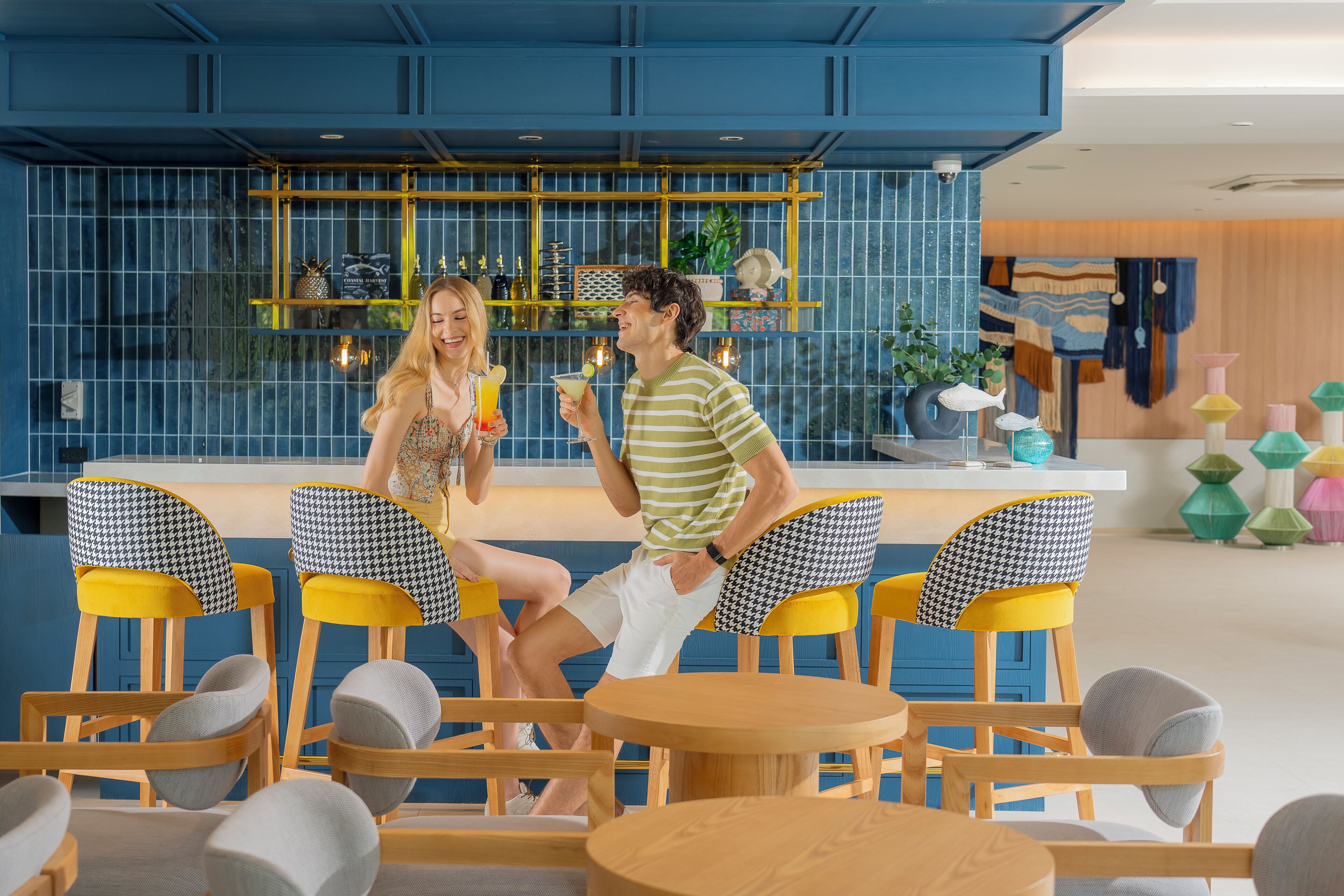 A modern bar area with blue walls, yellow and black checkered chairs, and wooden tables.