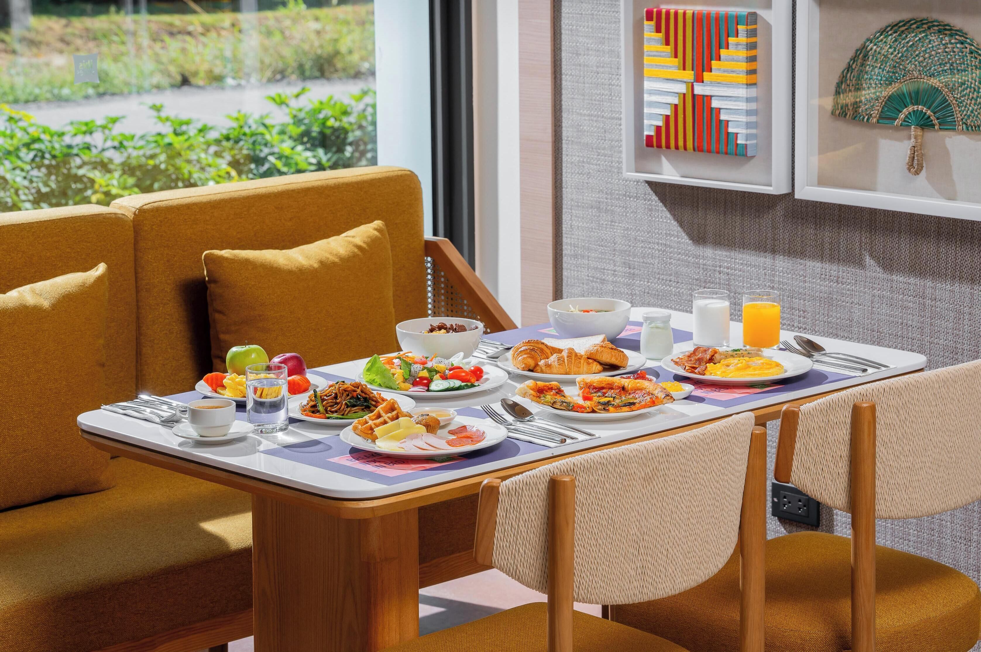 Une table dressée pour le petit-déjeuner avec différents plats, une vue sur la fenêtre et un mur agrémenté d’un objet décoratif.