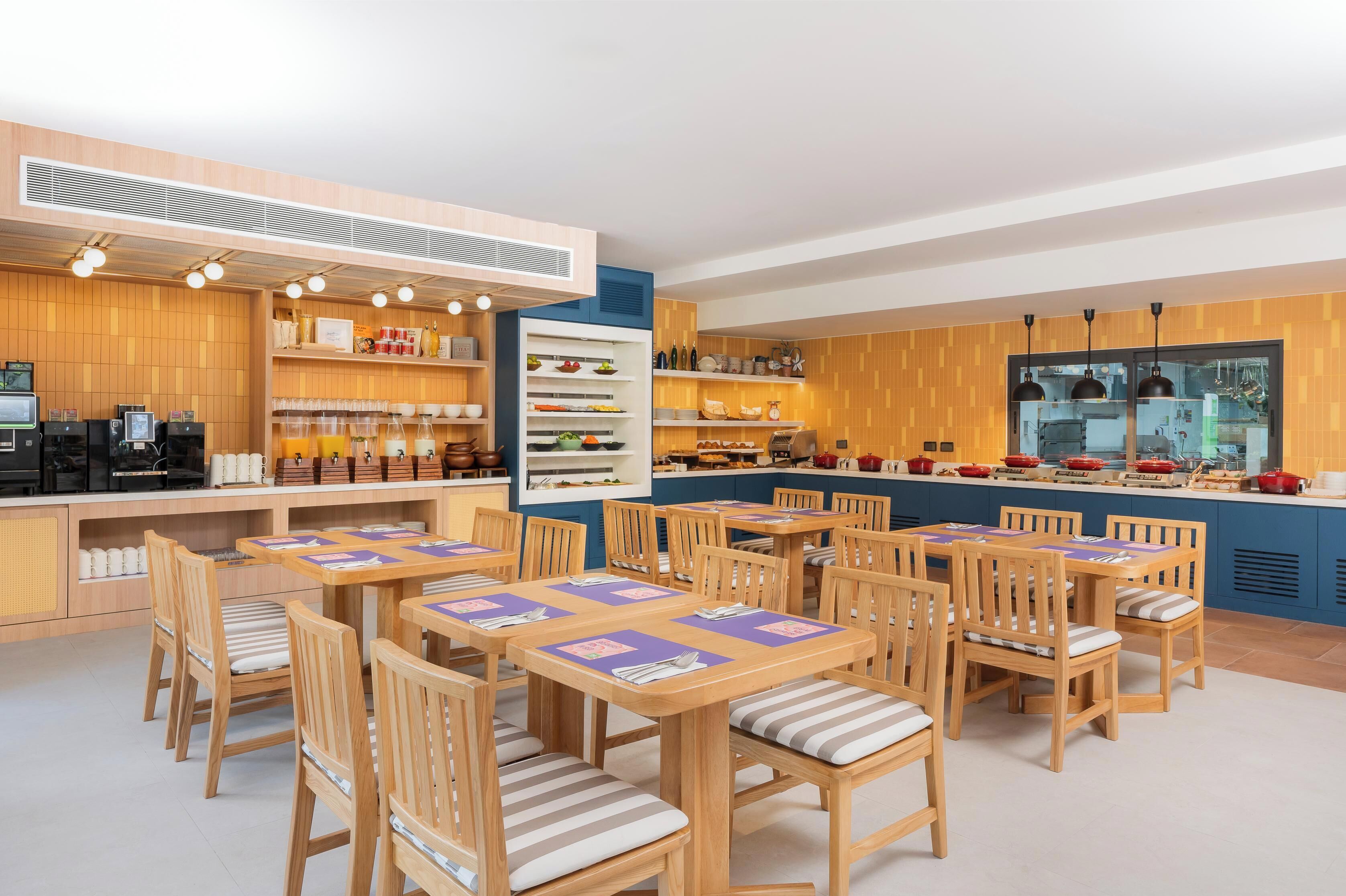 Un restaurante con mobiliario de madera, una zona de bufé y una cocina visible a través de un panel de vidrio.