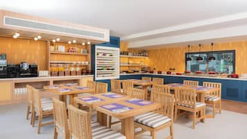 Un restaurante con mobiliario de madera, una zona de bufé y una cocina visible a través de un panel de vidrio.