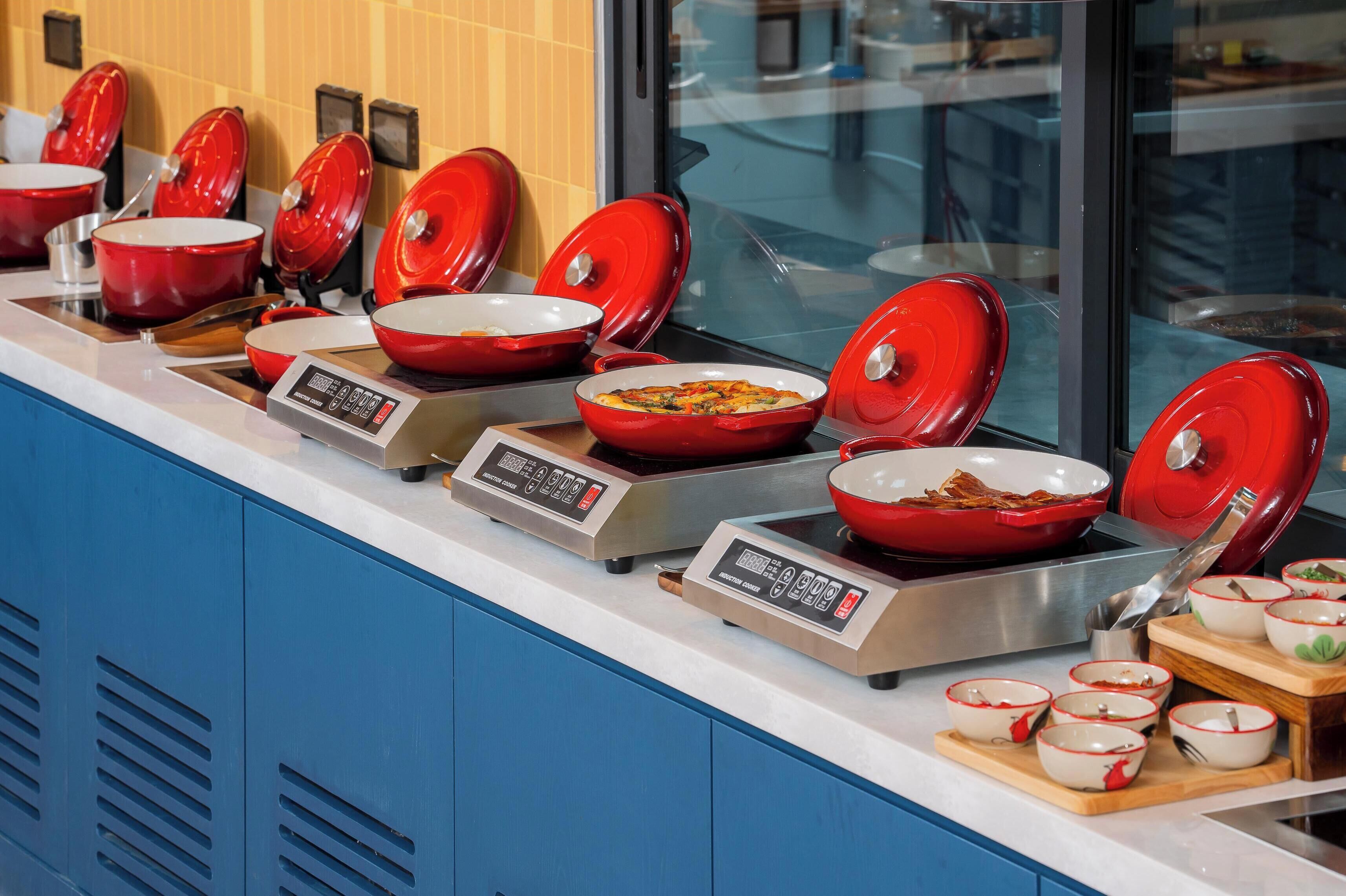 Un buffet avec de nombreux bols rouges disposés sur des plaques de cuisson à induction, un panneau de commande numérique et une variété de plats.