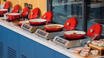 Un buffet avec de nombreux bols rouges disposés sur des plaques de cuisson à induction, un panneau de commande numérique et une variété de plats.