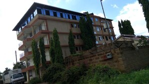 A multi-story building with balconies, a truck parked in front, and a stone wall with vegetation. - Market View Hotel Taveta (Taveta)