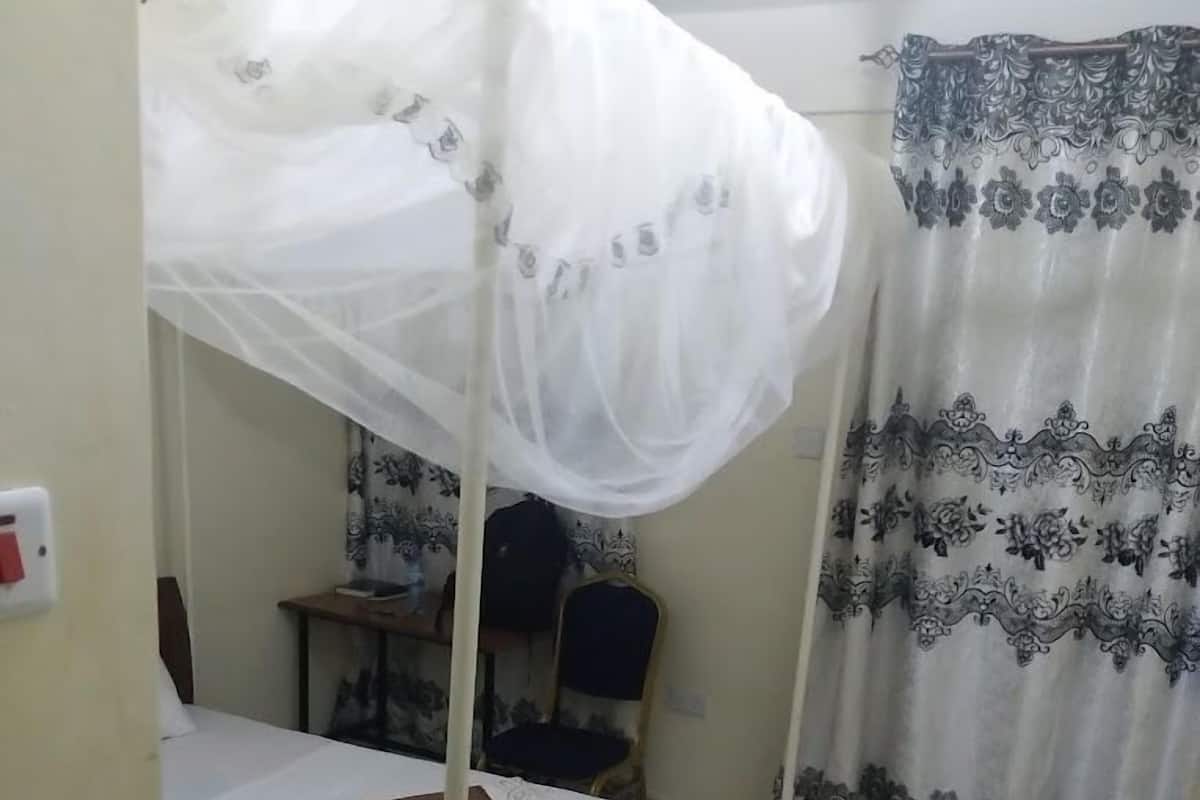 A bedroom with a single bed, a mosquito net, a desk, and a chair.