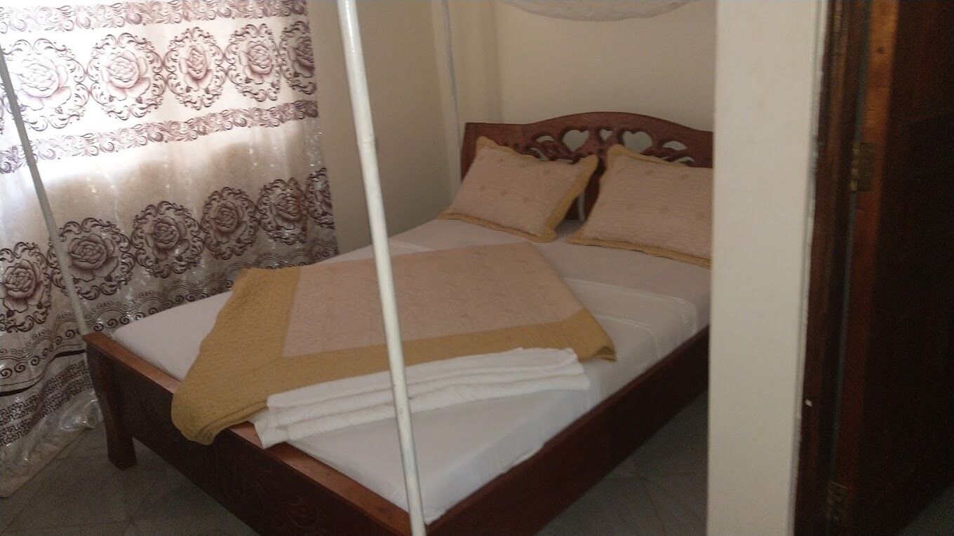 Uma cama bem arrumada com cabeceira de madeira, manta branca e um xale bege.