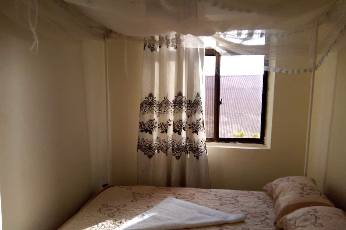 A bedroom with a bed, a window with curtains, and a view of the outside.
