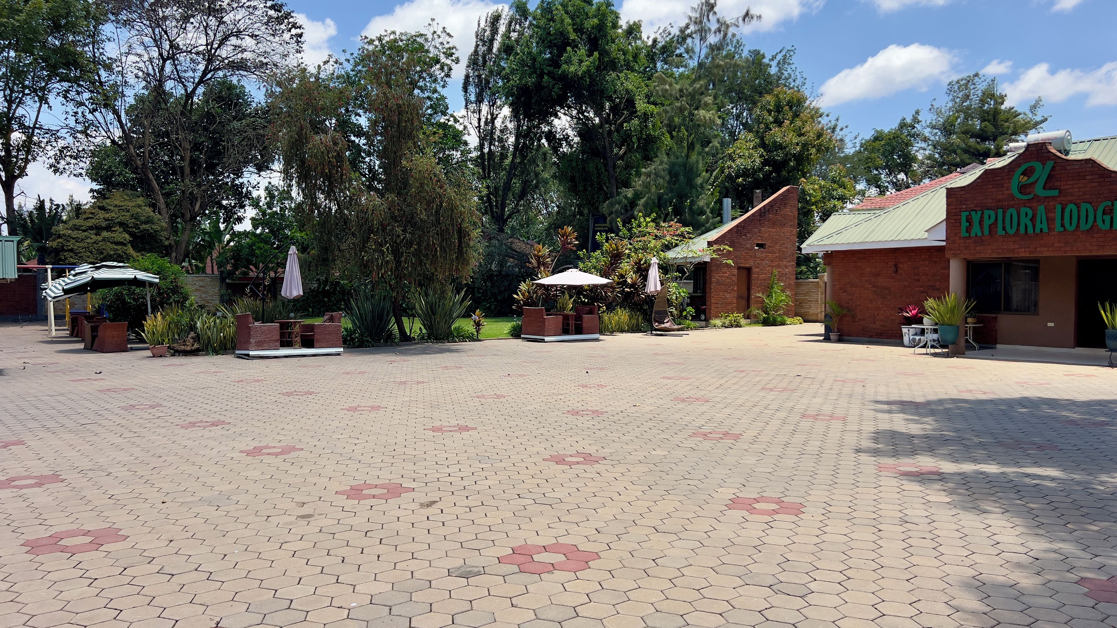 A paved courtyard with hexagonal tiles, outdoor seating, and a building with a sign reading 'EL EXPORIA LODGE'.