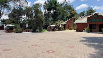 A paved courtyard with hexagonal tiles, outdoor seating, and a building with a sign reading 'EL EXPORIA LODGE'.