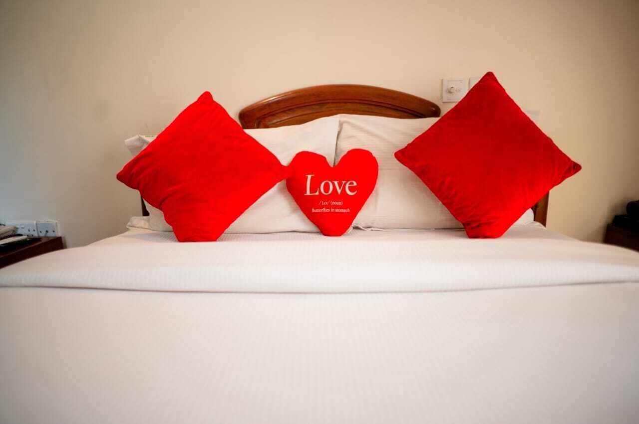 A bed with white bedding and three red pillows, one with the word "Love" on it.