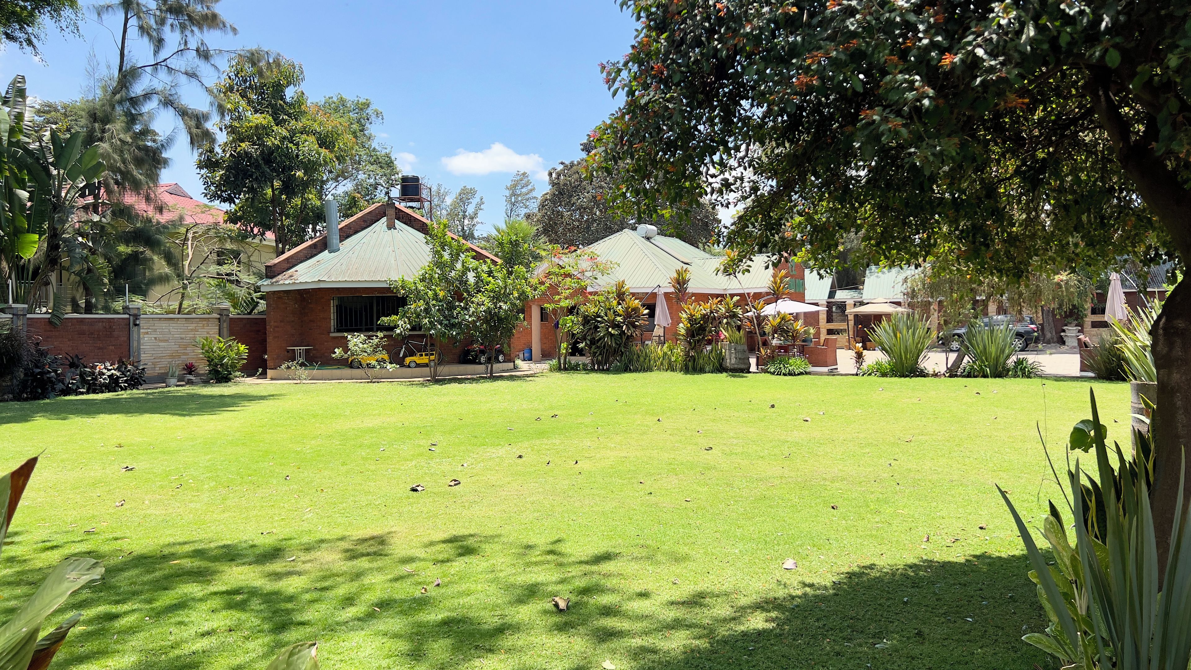 A residential property with a well-maintained lawn, a brick house with a green roof, and a garden area with various plants and trees.