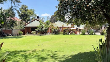 A residential property with a well-maintained lawn, a brick house with a green roof, and a garden area with various plants and trees.