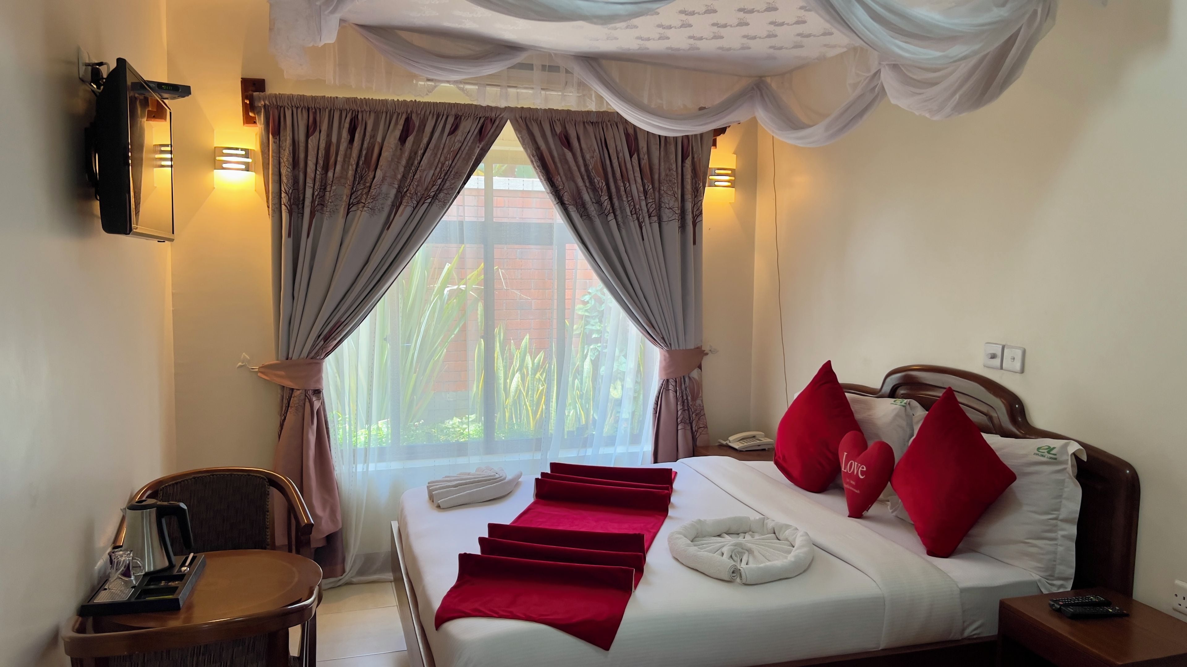 A hotel room with a bed, a bedside table, a chair, a desk with a telephone, and curtains.