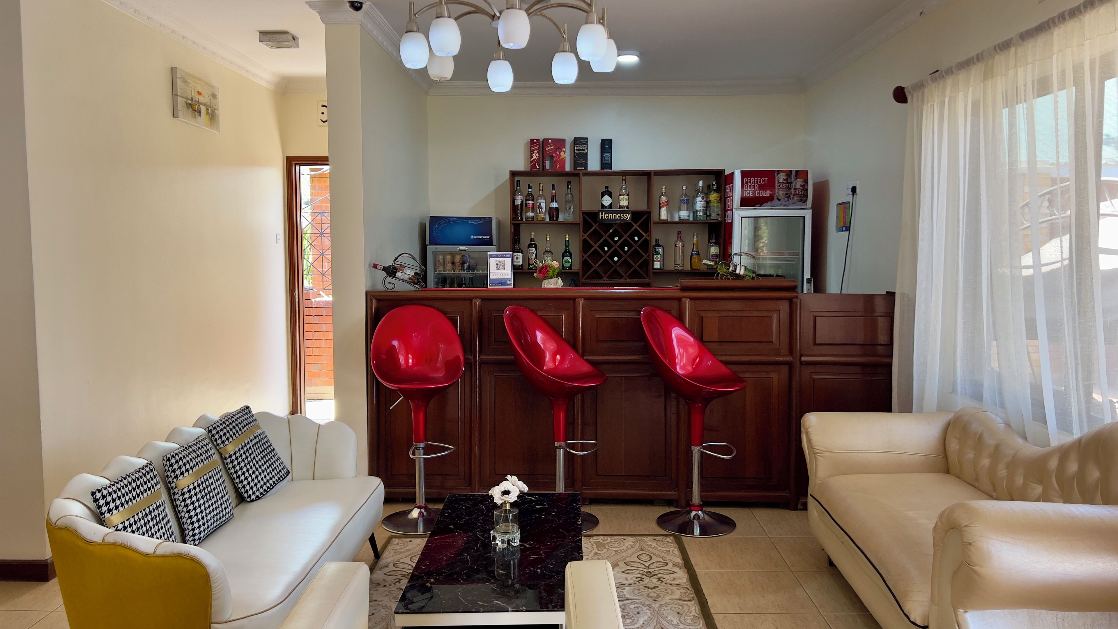 Un salon comprenant un canapé, une table basse et un coin bar avec des tabourets et des bouteilles.