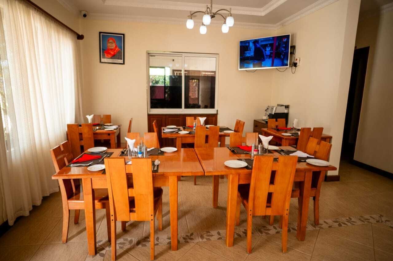 A dining area with wooden tables and chairs, a large window, and a television mounted on the wall.