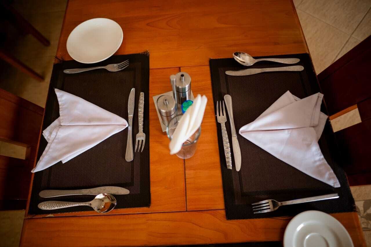Ein Esstisch mit zwei gedeckten Plätzen, jeweils mit gefaltetem Servietten, Besteck und Salz- und Pfefferstreuern.