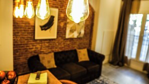 A living room with a brick wall, a dark-colored sofa, and hanging light fixtures. - Hotel Maruja in Cascorro. Madrid-Centro! 2 Bedrooms & private bathroom. A/C. Wi-Fi (Madrid)